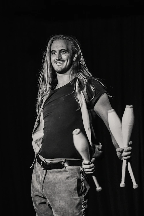 Charismatic juggler smiling with 3 juggling clubs in a silly pose