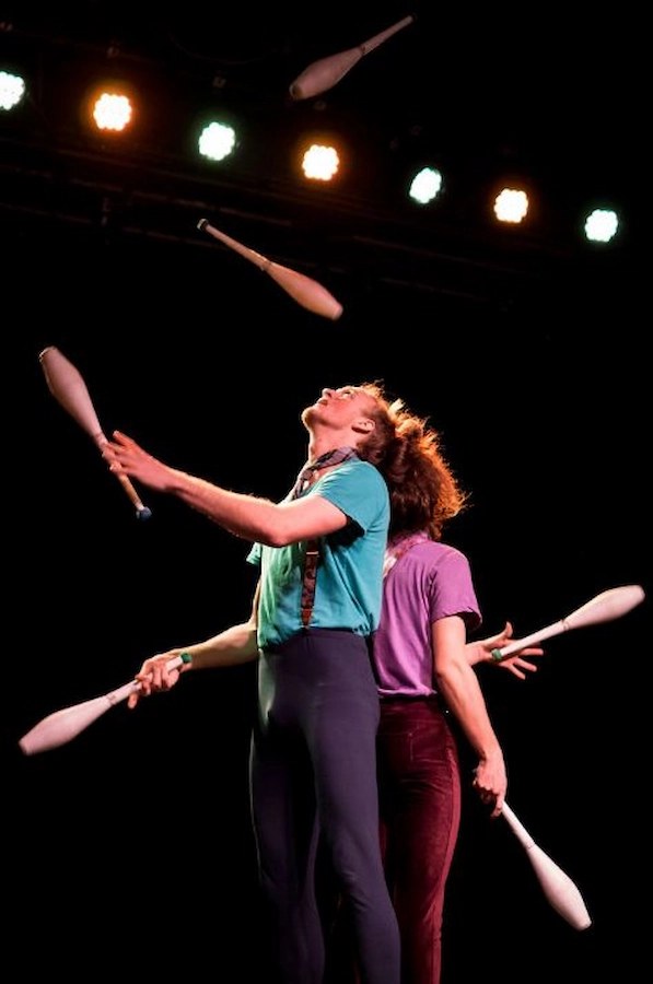 Circus performer passing many juggling clubs with partner