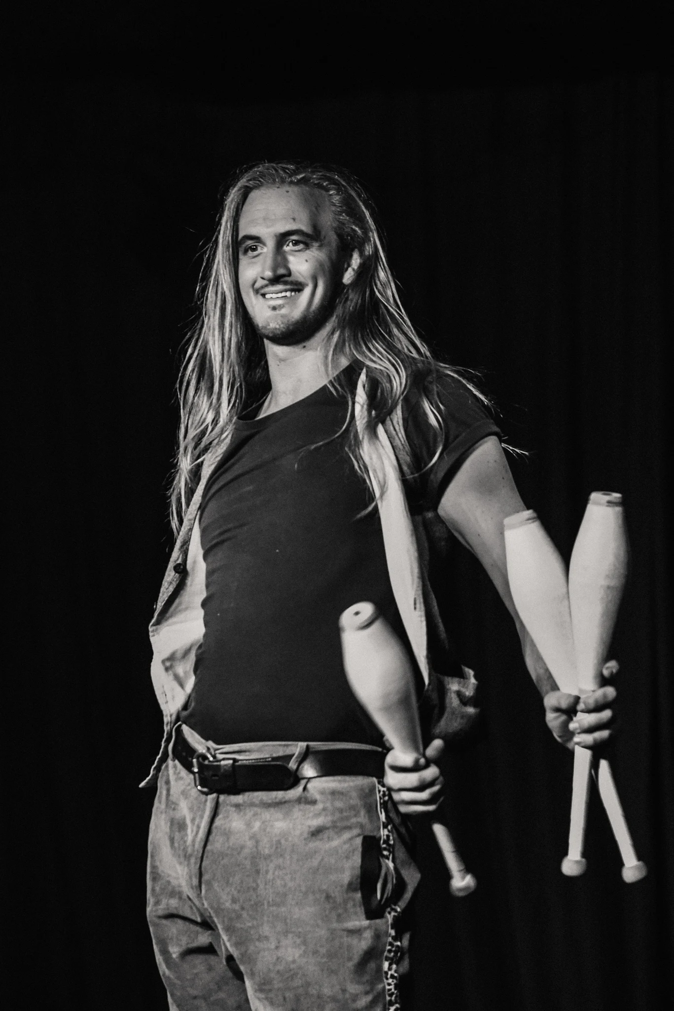 Charismatic juggler smiling with 3 juggling clubs in a silly pose