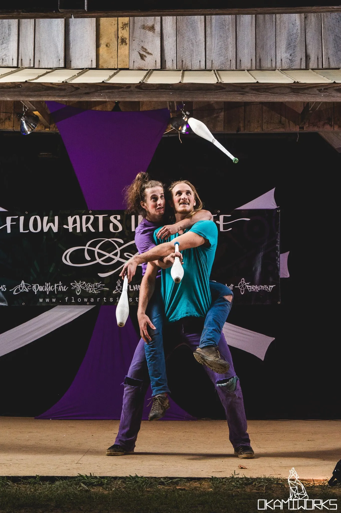Silly partner jugglers mounted on one another's backs performing at a flow festival