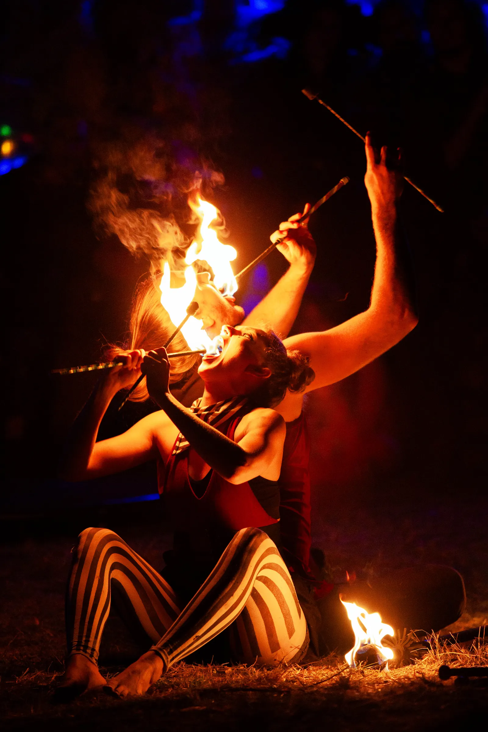 Fire performers eating fire sitting on ground back to back