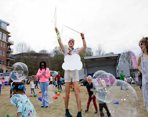 Man dressed as clouds and rainbows hosting a bubble play zone for children at a fair