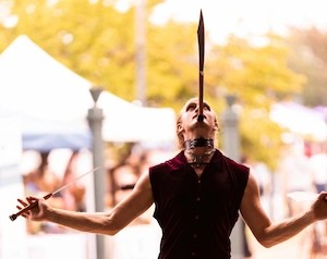 Performer balancing a knife on his face in gothic clothing