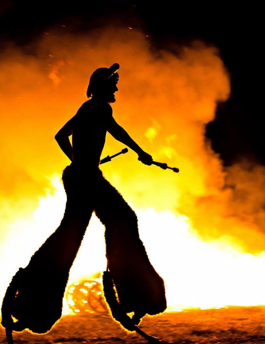 Faun character on stilts dancing with a massive fire in the background